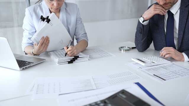 Professional auditors reviewing financial paperwork, using magnifying glass and calculator while analyzing business documents for detailed inspection and accounting compliance. Audit and taxes