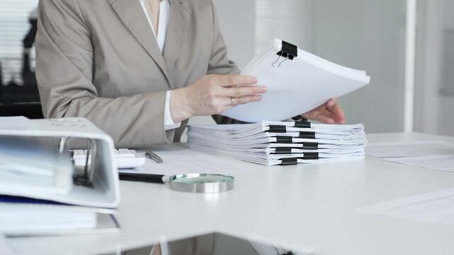 Businesswoman hands organizing stack of papers with binder clips, working on financial documents and official reports in office. Audit and taxes concept