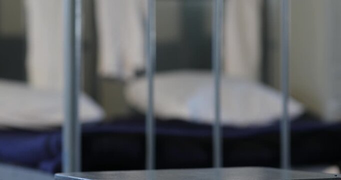 An unrecognizable soldier wearing camouflage pants is carefully tying the shoelaces of heavy black combat boots while resting one foot on a small stool in a barracks room.

