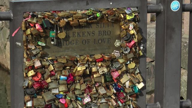 HELSINKI, FINLAND. The bridge of love and the railing with a memorial plate and padlocks on a bright summer day.