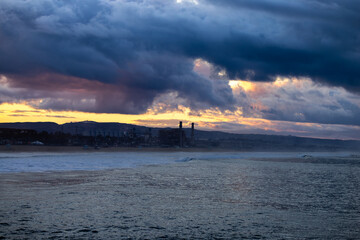 Obraz premium Dramatic sunrise and dark storm clouds over a coastal power plant at the edge of the Pacific Ocean