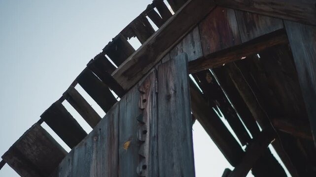 Weathered barn rafters with deep shadow, closeup of aged wood planks and exposed nails, gritty grain and cool toning, architectural study of decay suggesting documentary or restoration planning.