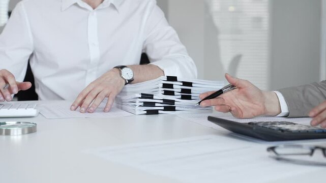 Professionals handling a large stack of documents and paperwork, signing a contract in a busy office. Audit and taxes in business