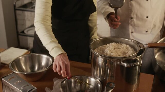 High angle tilt up shot of three middle aged women cooking rice and frying vegetables with chef during cooking master class in restaurant