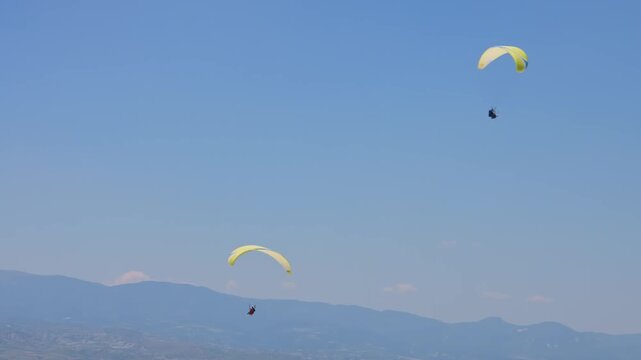 Two paragliders drift gracefully through a clear, vibrant blue sky above the majestic mountain ranges of Turkey. This wide-angle shot captures the essence of extreme sports, freedom, and adventure tou