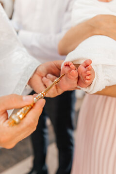 A close-up of a priest using a golden brush for the holy anointing ritual on a newborn baby's feet during a traditional Orthodox christening.