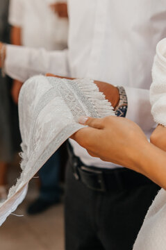 Close-up of hands holding a white embroidered baptismal towel (kryzhma) with a cross and dove, and a priest holding a prayer card during the ceremony.