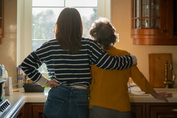 Daughter and her old mother stands near the window and hugs. © Zhanna