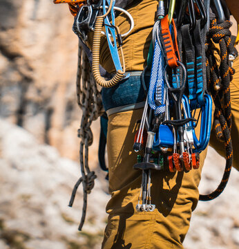 Mountaineering gear with carabiners, ropes, belay devices on a young man closeup.