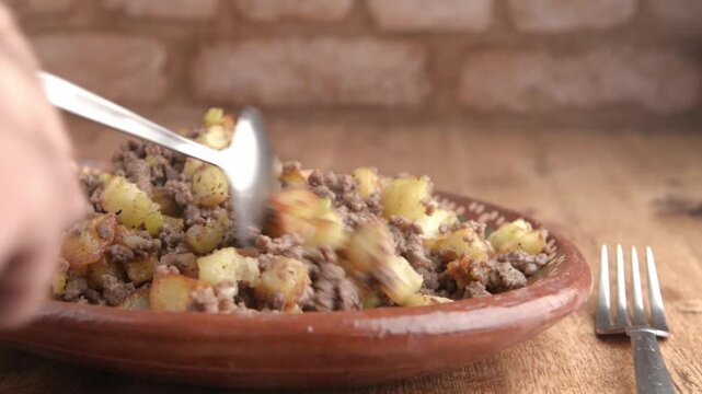 picadillo con papas,servido en un plato Mexicano de barro vista lateral con fondo de pared de ladrillos rusticos, imagen con acercamiento o zoom.