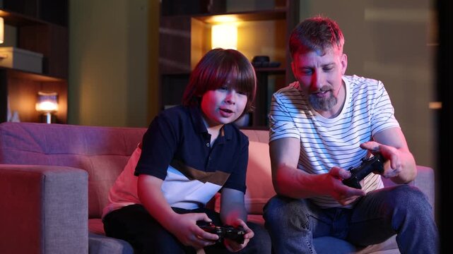Happy father and son with controllers playing video game on sofa at home