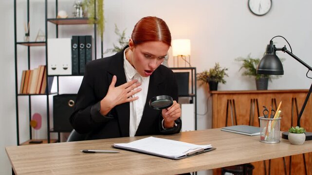 Young businesswoman at home office inspects contract through magnifying glass spots commission and scowls. Freelancer girl at table confronts fee clause demanding change angered by unfair extra cost