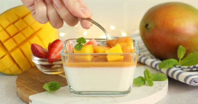Woman eating delicious mango panna cotta at light grey table, closeup