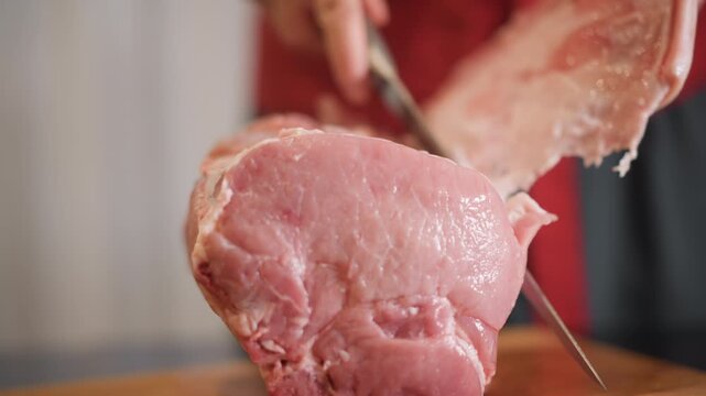 Home cook removing fat from pork joint on cutting board, steady hands peeling membrane and trimming exterior, closeup of blade angle and control, clinical bright kitchen light, skillful prep
