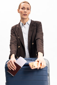 Young woman in brown jacket holds suitcase, passport, and smartphone, preparing for travel. Isolated on white background, concept of business trip, vacation, and journey preparation.