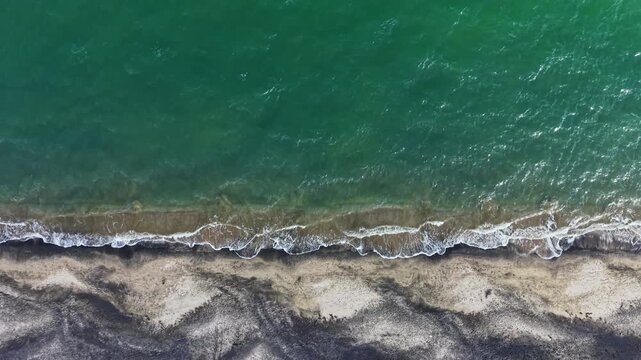 Water splashes onto sand along the coastline. The ocean is blue while the shore has darker patches. This scene captures the natural beauty of the beach.