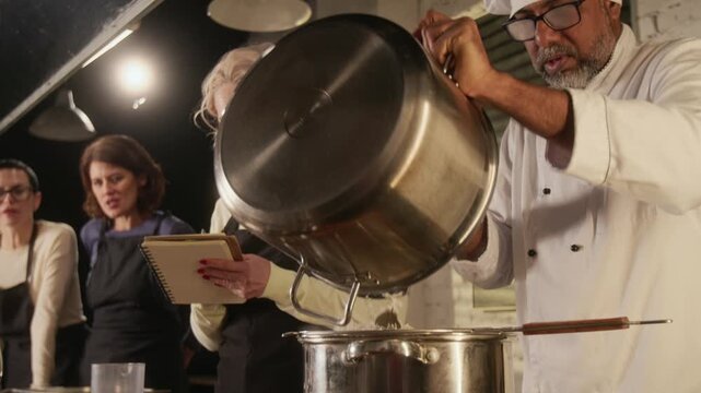Low angle shot of biracial chef straining cooked rice into metal pan during group cooking master class in restaurant