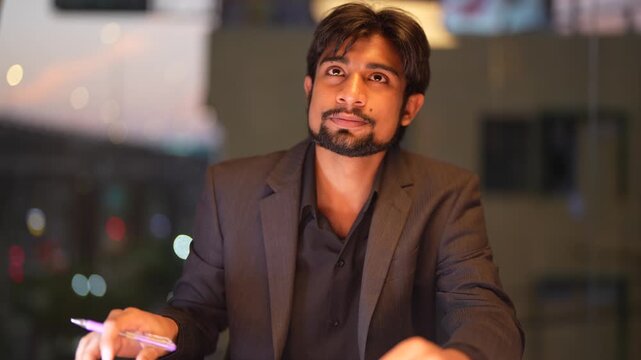 Skilled Indian technical consultant scrutinizing complex analytical reports with illuminated skyscraper views in the background within a high end corporate environment.