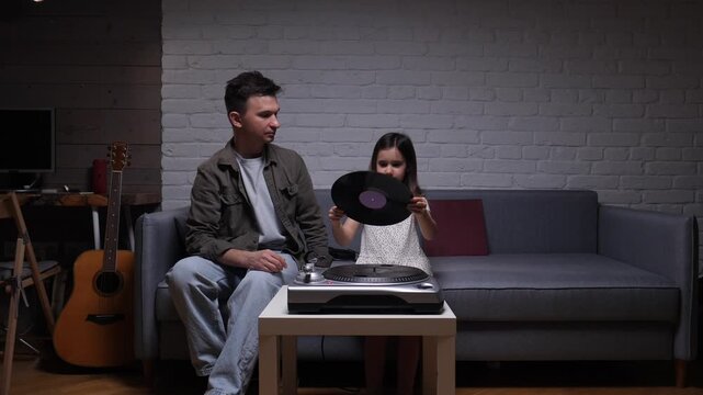Caring father showing his young daughter how to use a record player at home, sharing vintage music and creating meaningful family bonding moments together in a cozy living room