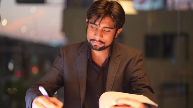 Poised South Asian IT director scrutinizing complex analytical reports against a sparkling city nightscape while demonstrating professional expertise highlighting professional authority and focus.
