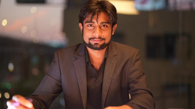 Skilled Indian technical consultant reviewing cloud infrastructure metrics against a sparkling city nightscape while demonstrating professional expertise highlighting professional authority and ...