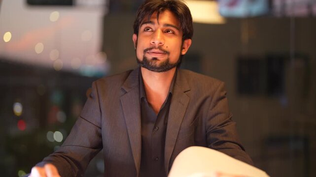 Poised South Asian IT director preparing comprehensive technical strategies featuring a panoramic urban skyline at dusk displaying assertive leadership and expertise.