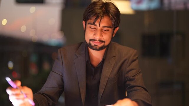 Experienced Indian engineering lead facilitating global digital transitions overlooking a vibrant metropolitan night scene inside a sophisticated executive workspace.