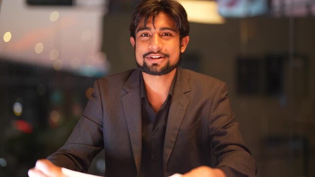 Assertive Indian software architect scrutinizing complex analytical reports with illuminated skyscraper views in the background within a high end corporate environment.