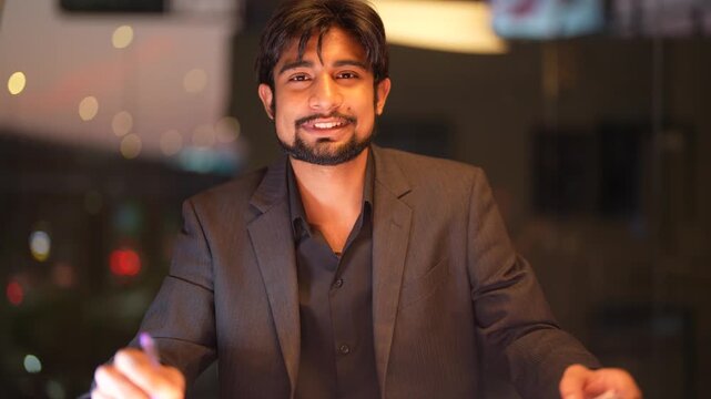 Experienced Indian engineering lead scrutinizing complex analytical reports against a sparkling city nightscape while demonstrating professional expertise highlighting professional authority and...