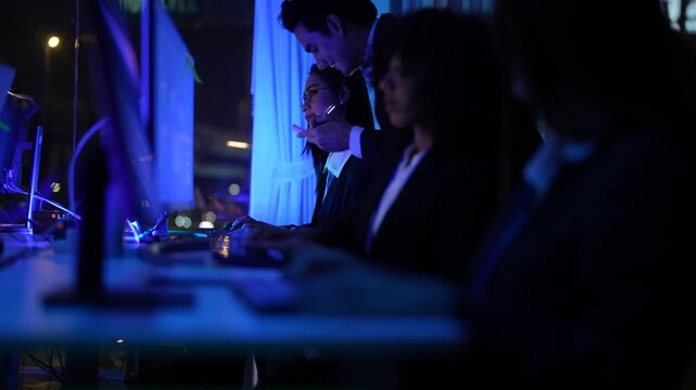 Poised cross functional specialists featuring senior male executive and young female analyst overseeing complex electronic systems and software code at a high tech operations center at night.