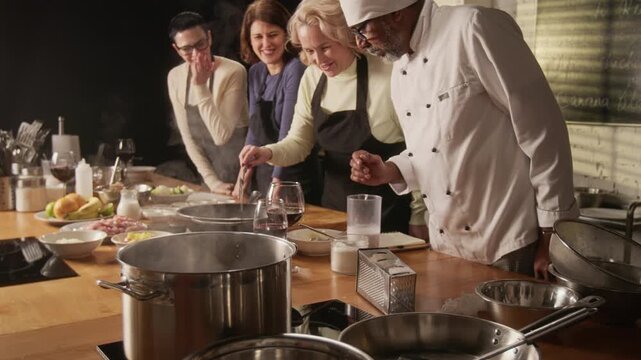 Low angle tilt up shot of group of women cooking while male chef teaching and helping them during cooking master class in restaurant