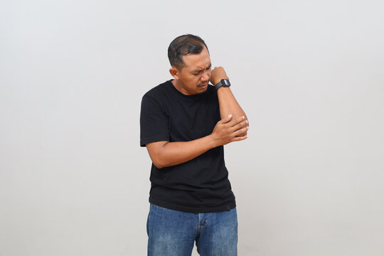 A man stands isolated on a white background with pain in his elbow.