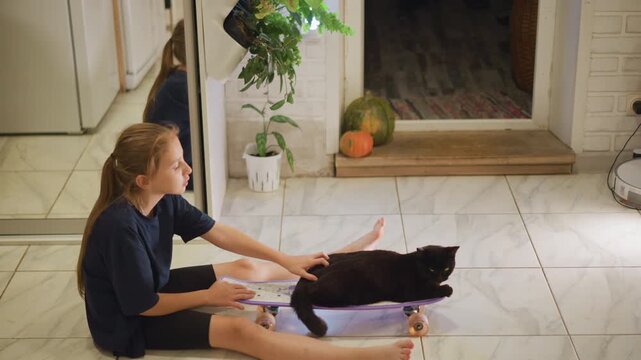 White girl reaching toward black cat on kitchen floor playful gentle touch, potted plant and doorway in background, barefoot child exploring pet bond and casual domestic interaction in home kitchen.