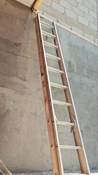 Wooden ladder leaning against a tall concrete wall at a construction site