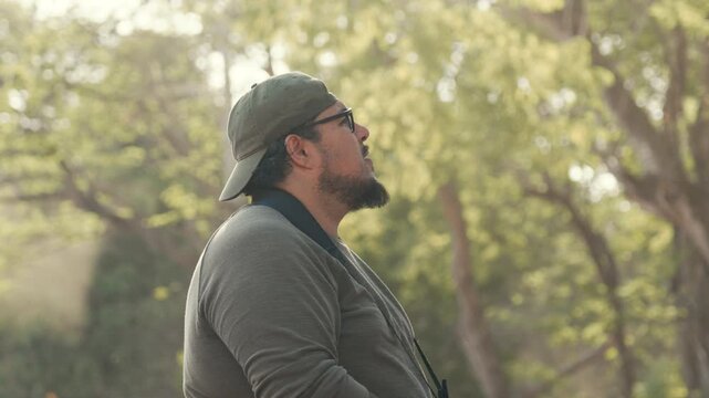 Birdwatcher man using binoculars in a sunny forest