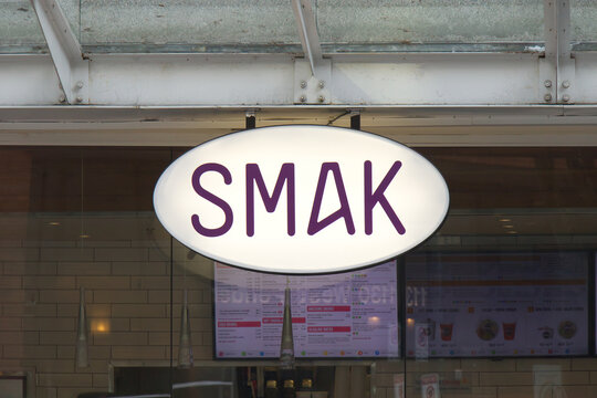Illuminated oval SMAK restaurant sign with purple lettering hanging outside the healthy fast casual eatery in downtown Vancouver.