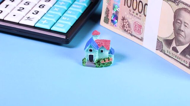 水色背景で回転する札束とミニチュアハウスと電卓の映像