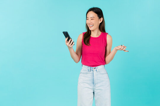 Happy smiling young Asian woman holding smartphone on blue background.