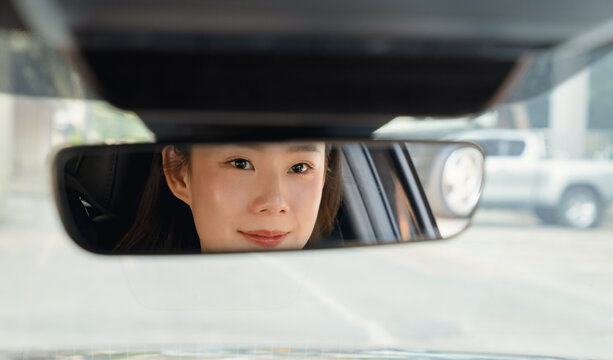 Woman glances into the rearview mirror with smile, feeling confident and ready for the journey ahead.
