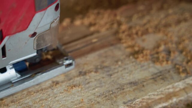 Jigsaw cutting wood plank across workshop surface, professional carpenter guiding blade, shavings scattering, red power tool in motion, focused on edge and speed, gritty construction atmosphere