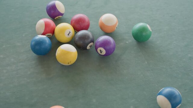 Billiard balls on green felt clustered in triangle rack then scattering after break colorful numbered solids and stripes rolling across textured table surface overhead closeup capturing motion,