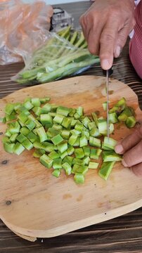 Hands slicing fresh nopal cactus paddles on a wooden cutting board