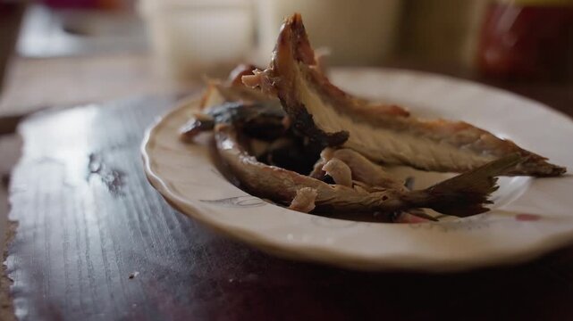 Dried anchovies on wooden table, carpentrymade surface with porcelain plate and warm afternoon light. Salt crystals cling to crispy flesh, closeup texture of scales and rim, rustic home snack hinting