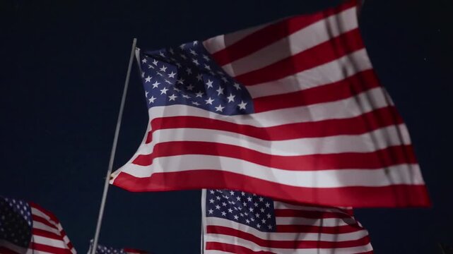 Close American flag waving in wind at night in Malibu, California, USA illuminated by strong lights, creating dramatic patriotic and emotional remembrance atmosphere
