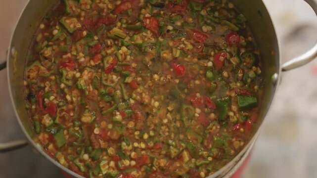 Overhead pot finishing chunky vegetable stew with spoon tomatoes, peppers and okra meld into thick relish, final stirring and tasting gestures, warm cozy atmosphere, steaming aroma and homestyle