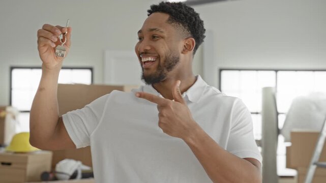 Man holds key in raised hand and points finger to key inside a building with packed moving boxes, ladder and hardhat; moving day joy.