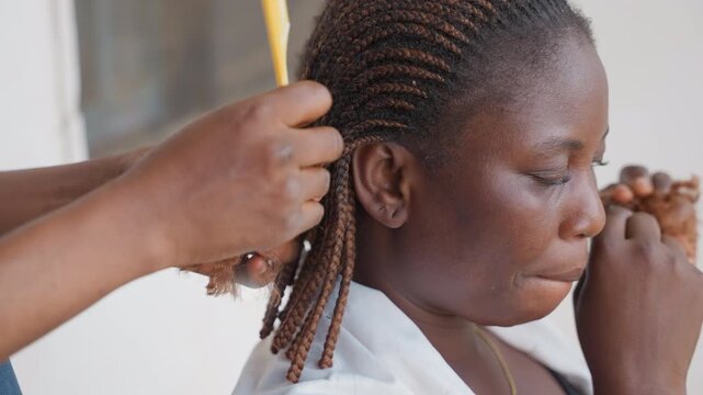 Woman carefully styles cornrow braids. Patient woman styling her hair with care and focus. Woman with cornrows carefully and tenderly maintains her intricate hairstyle with attention