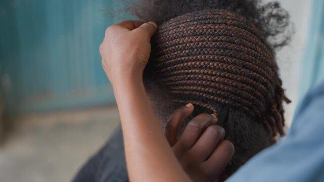 Closeup braided hair being tucked with careful stylist hands, neat cornrows hugging scalp, teal doorway backdrop, patient finishing, precision and texture emphasized, community salon atmosphere,
