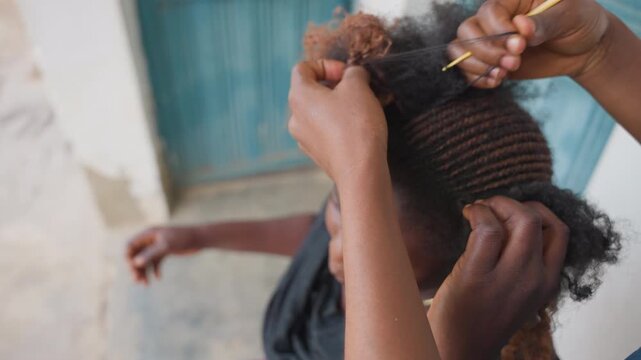 Close black apprentice measuring hair part, comb aligning neat rows across scalp outdoor street setting, focused technique, careful tension, fingers guiding braided pattern, tutorial energy