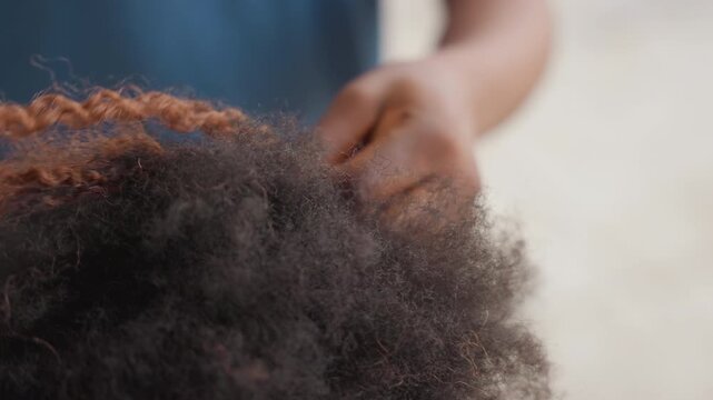 Close up hands braiding natural hair, stylists fingers weave tight braid along textured coils and strands, intimate salon scene with soft natural light, slow focused motion, visible dust particles,